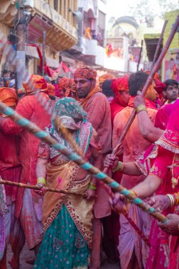 Barsana, Uttar Pradesh, Hindistan - Mart 2022: Barsana 'lı Hindu kadınlar ellerinde peçeleri ve bambu çubuklarıyla erkek insanları Nandgaon' dan geleneksel lathmar holi ritüeli olarak yeniyorlar.