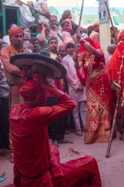 Barsana, Uttar Pradesh, Hindistan - Mart 2022: Barsana 'lı Hindu kadınlar ellerinde peçeleri ve bambu çubuklarıyla erkek insanları Nandgaon' dan geleneksel lathmar holi ritüeli olarak yeniyorlar.
