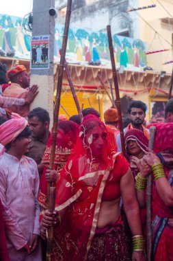 Barsana, Uttar Pradesh, Hindistan - Mart 2022: Barsana 'lı Hindu kadınlar ellerinde peçeleri ve bambu çubuklarıyla erkek insanları Nandgaon' dan geleneksel lathmar holi ritüeli olarak yeniyorlar.