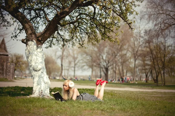 Blond meisje liggen onder een boom met boek — Stockfoto