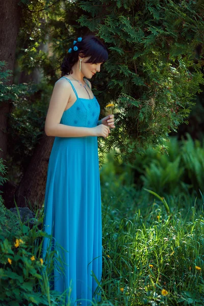 Mädchen in blauem Kleid steht neben einem Baum. — Stockfoto