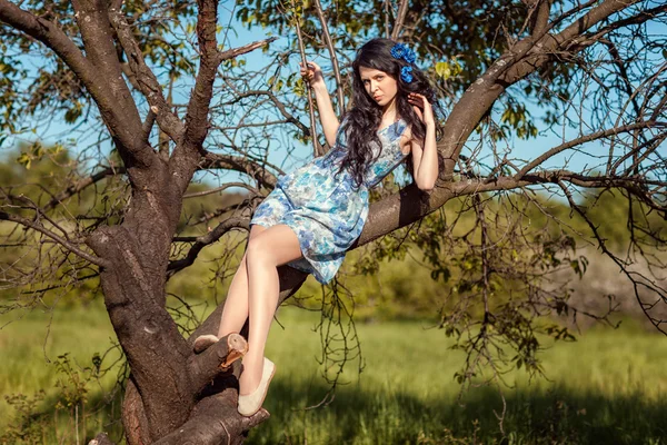 Beautiful brunette girl sitting on a tree. — Stock Photo, Image