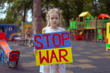 Ukrainian girl child asks to stop the war. In her hands board stop war.
