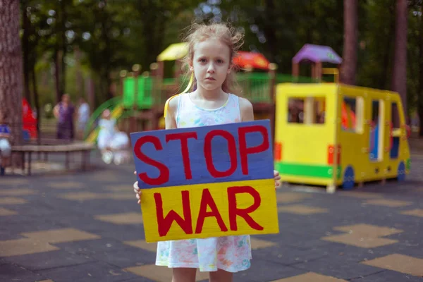 Ukrainian girl child asks to stop the war. In her hands board stop war.