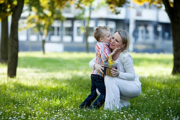Beautiful boy and mom in spring park with present. Mothers day or birthday celebration concept — Stock Photo, Image