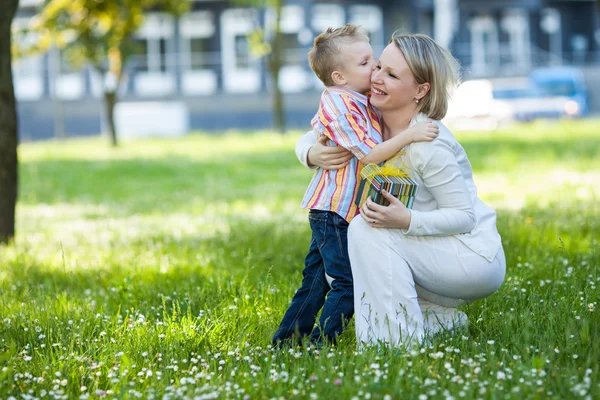 Anak laki-laki dan ibu yang cantik di taman musim semi dengan hadiah. Ibu hari atau ulang tahun konsep perayaan — Stok Foto