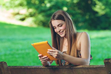 güzel bir genç kadın tablet ile parkta bankta oturmuş