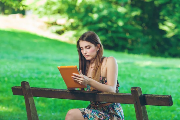 Hermosa joven sentada en el banco en el parque con la tableta — Foto de Stock