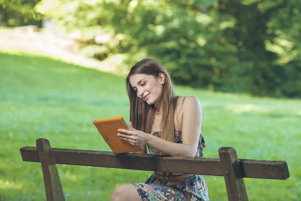 Gyönyörű fiatal nő ül a padon, Park, tabletta — Stock Fotó