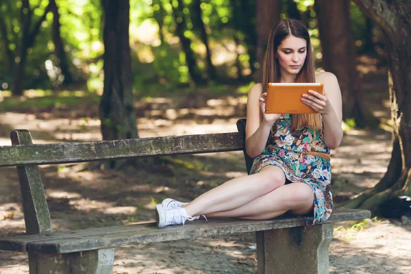 Güzel bir genç kadın tablet ile parkta bankta oturmuş — Stok fotoğraf