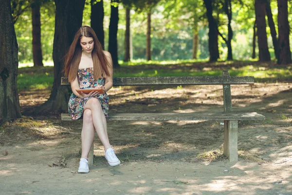 Hermosa joven sentada en el parque con la tableta — Foto de Stock