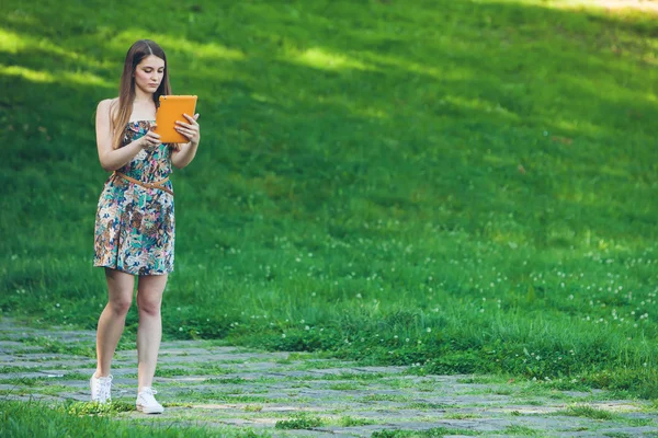 Красива молода жінка сидить в парку з планшетом — стокове фото