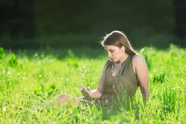 Hermosa joven en el parque escuchar música en el teléfono inteligente — Foto de Stock