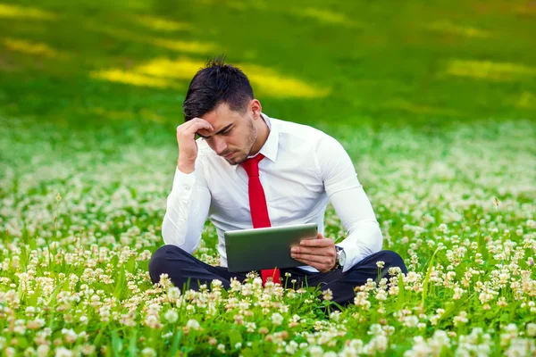 Concerned young business man sitting in city park holding computer tablet — Stock Photo, Image