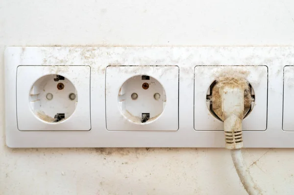 dirty dust on the power socket or connector and electric wire in the room. real old neglected dusty dirt on the electrical computer wire and white wall in the home in the apartment close up
