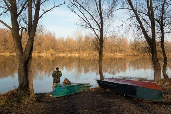 Kamuflaj pantolonu ve kapüşonlu ceketli bir adam sonbahar sabahı nehirde balık tutuyor..