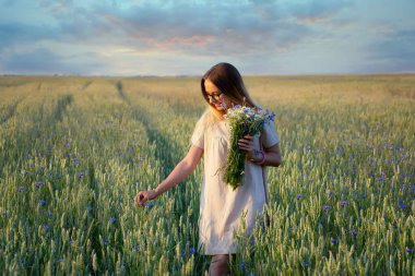 Gün batımında çiçek tarlasında gülümseyen güzel sarışın kadın, elinde buketle şehvetli tatlı bir bayan..