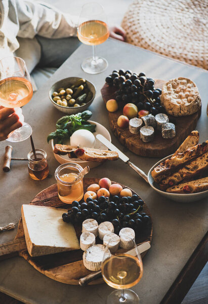 Glasses with orange or rose wine and various gourmet snacks cheese grape bread for company of friends on concrete background. Gathering, celebrating, wine tasting concept