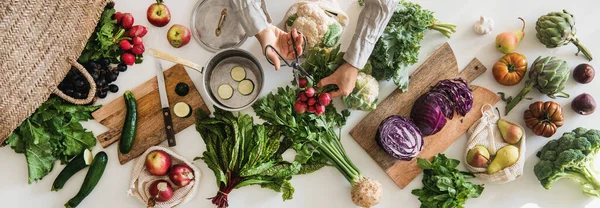 Fall vegetarian cooking background. Female hands cutting ingredients for cooking over table with fresh seasonal vegetables, greens, fruit from grocery market, top view. Vegan, healthy, organic food