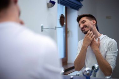 Nadir sakallı adam banyo aynasına dokunmuş gibi bakıyor.