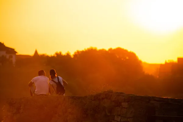 Bir çift genç gün batımında uçurumun kenarında oturuyor.. — Stok fotoğraf
