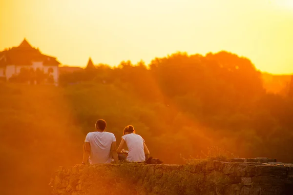 Bir çift genç gün batımında uçurumun kenarında oturuyor.. — Stok fotoğraf