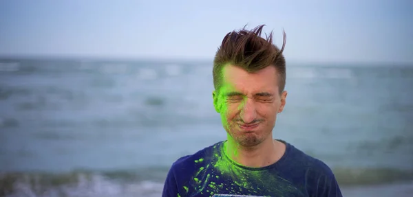 A young guy throws colour powder against the background of the sea — Stock Photo, Image