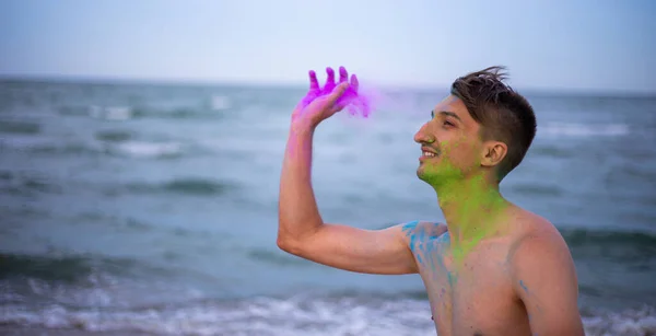 Ένας νεαρός ρίχνει σκόνη χρώματος στο φόντο της θάλασσας. — Φωτογραφία Αρχείου