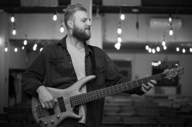 A young guy with a beard plays a bass guitar with five strings