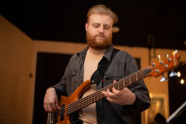 A young guy with a beard plays a bass guitar with five strings