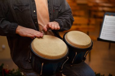 A young guy with a beard plays percussion bongos