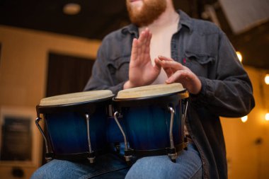 A young guy with a beard plays percussion bongos