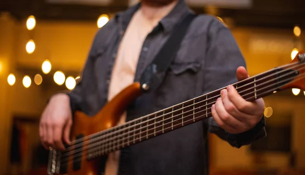 A young guy with a beard plays a bass guitar with five strings — Stok fotoğraf