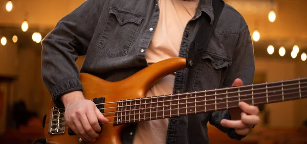 A young guy with a beard plays a bass guitar with five strings — 图库照片