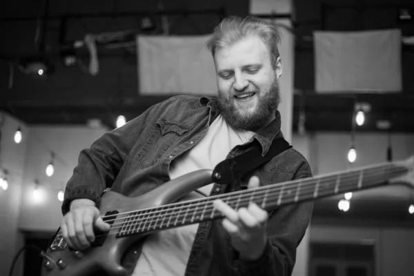 A young guy with a beard plays a bass guitar with five strings — Fotografia de Stock