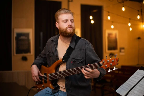 stock image A young guy with a beard plays a bass guitar with five strings