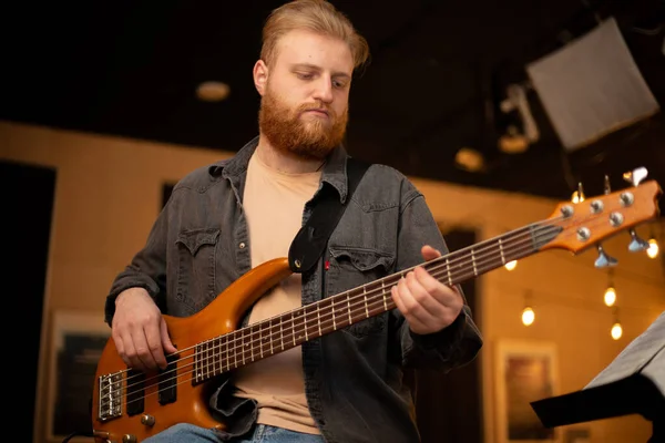 A young guy with a beard plays a bass guitar with five strings — Stockfoto