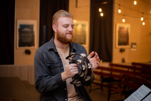 A young guy with a beard plays the tambourine