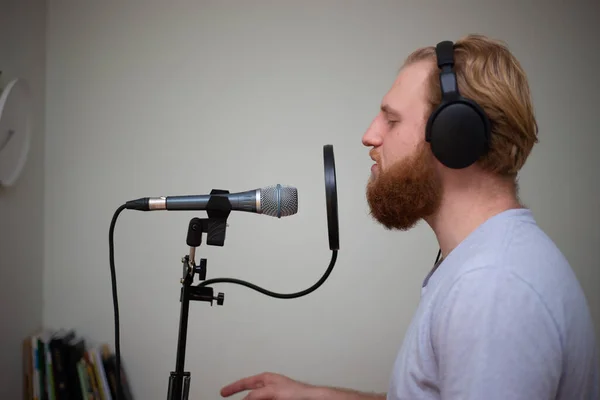 Ένας νεαρός με γενειάδα τραγουδάει σε ένα μικρόφωνο στούντιο με ποπ φίλτρο. — Φωτογραφία Αρχείου