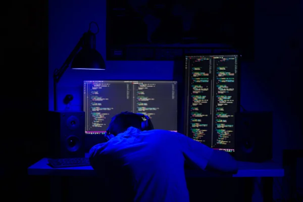 Een man slaapt achter een computer in een kamer aan een tafel 's nachts met blauwe verlichting en programma' s — Stockfoto