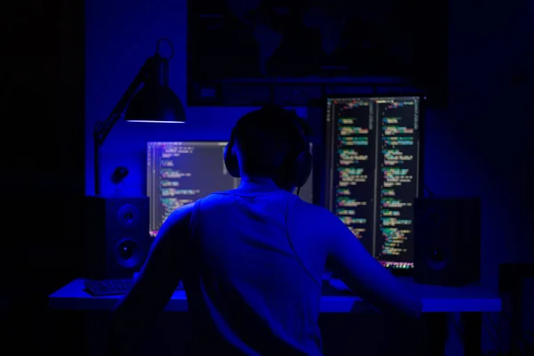 Een man zit 's nachts aan een computer in een kamer aan een tafel met blauw licht en programma' s — Stockfoto