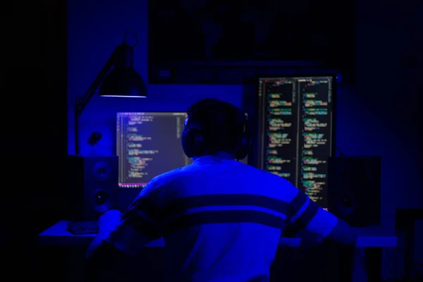 Een man zit 's nachts aan een computer in een kamer aan een tafel met blauw licht en programma' s — Stockfoto