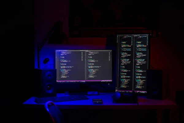 Un uomo si siede a un computer in una stanza a un tavolo di notte con illuminazione blu e programmi — Foto Stock