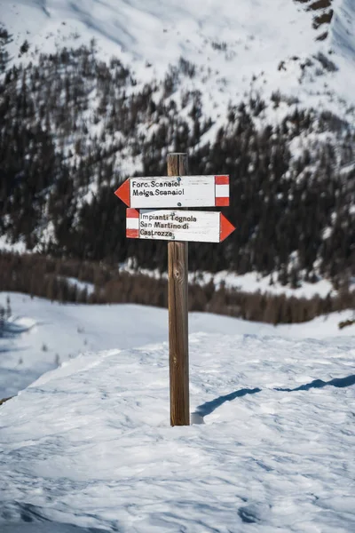 Dolomitlerdeki San Martino di Castrozza 'nın karlı manzarasında kırmızı okları olan, farklı yönleri gösteren eski bir tahta tabela.