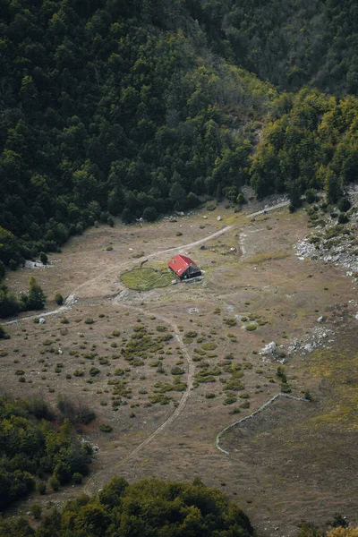 Arnavutluk 'un lanetli dağlarındaki bir ormanın ortasında harap olmuş kırmızı çatılı terk edilmiş eski bir ahşap ev yukarıdan görüldüğü üzere