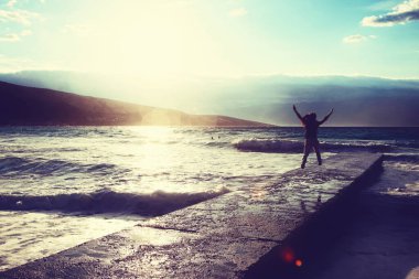 Özgürlük duygusu konsepti. Kadın büyük dalgalarla denize bakan iskelede zıplıyor.