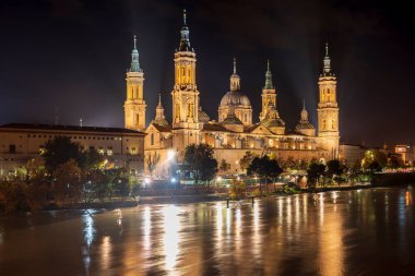 Bazilika del Pilar aydınlandı ve gece Ebro Nehri şehrin içinden geçerken yansıdı. Uzun pozlu çekim. Zaragoza, İspanya