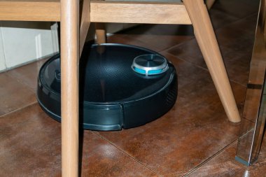 Yerleri temizlerken sandalyelerin arasına sıkışmış akıllı robot süpürgesi.