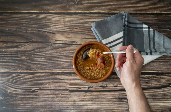上方是一只手拿着一只小扁豆勺的手 从土盘子里拿出来放在一个乡村木桌上 上面有文字的空间 健康和传统的西班牙烹饪概念 — 图库照片
