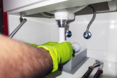 Musluk tamir eder ve lavabonun altındaki hortumu korur. Banyoda çalışan tesisatçı, tesisat kurulumu ve kurulum konsepti.